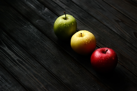 Red green yellow apples in a diagonal row with water drops on black wooden table, back light. Backgroundの写真素材