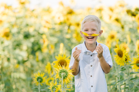Adorable toddler blond boy in a shirt on sunflower field laughing and having fun outdoors. Life style, summer time, real emotions. Kid portrait. Summer countryside agricultureの写真素材