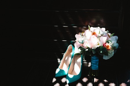 Bridal bouquet of pink peonies and mint tape, high heels shoes on dark background with harsh shadows. Wedding floristic compositionの写真素材