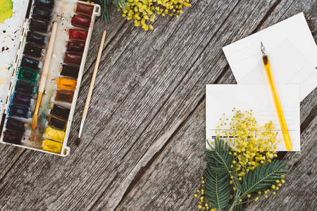 Workspace. Wreath frame with mimosas, watercolors, pen ink and vintage postcard on wooden background. moke upの写真素材