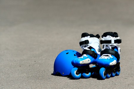 Roller inline skates with helmet in skate park on gray asphalt background. Street culture,...
