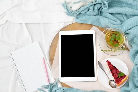 Flat lay breakfast in bed with raspberry cheesecake, mint tea and open note book, tablet. Window light, space for text blog, postsの写真素材