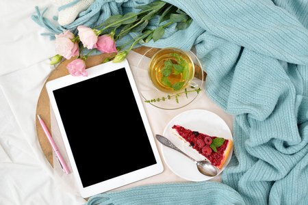 Flat lay breakfast in bed with raspberry cheesecake, mint tea and open note book, tablet. Window light, space for text blog, postsの写真素材