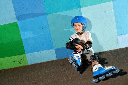 Cute little athletic boy on roller skates sitting against the blue graffiti wall. Rollerblading...