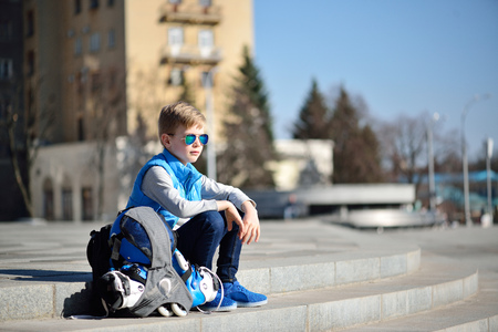 Young boy sitting near grey wall with inline roller skates and all protection at outdoor skate parkの写真素材