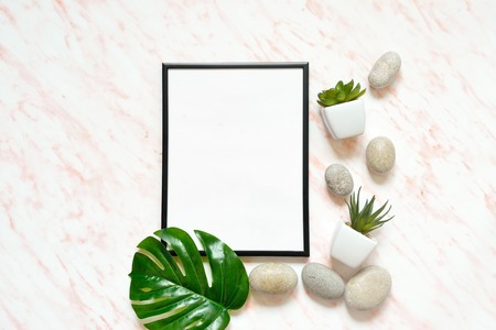 Flat lay marble desk with white empty frame for text, stones and succulents background