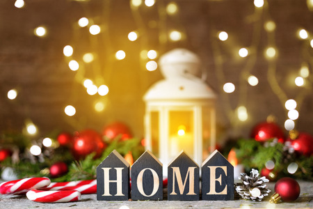 Christmas composition with and Shining lights. Red balls, Pine cones, lollipop, toy houses text Home on Wooden Tableの写真素材