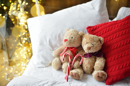 Two teddy bears siting on the bed with red candys near christmas tree.の写真素材