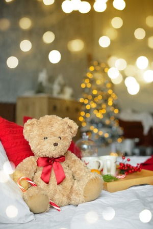 Two teddy bears siting on the bed with red candys near christmas tree.の写真素材