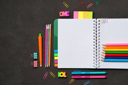 Back to School concept - open copy book with office and student supplies on black chalk background....