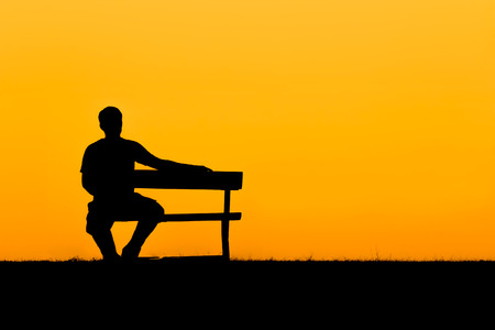 A silhouette of man sitting on bench and him looking at the sky in sunset