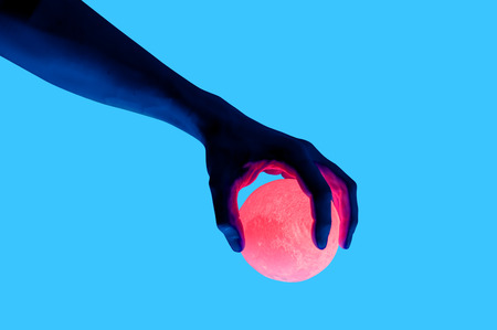 Isolated on blue background photo of man holding moon shape illuminated sphere. Surrealistic collage style, contemporary art element for design, posters and banners. Neon purple light. Pop inspirationの写真素材