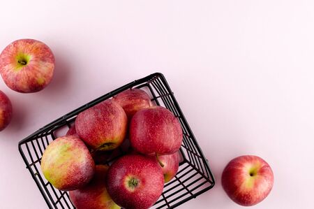Red apples in the metallic black basket on the light pink background. Top view flat lay composition. Space for text template. Fresh autumn fruit wallpaper.の写真素材