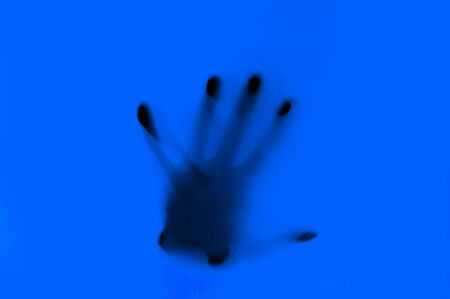 Hand in blue neon light behind transparent surface. Foggy blurred effect for different concept ideas. Trendy bold illumination. Abstract backgroundの写真素材