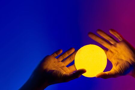 Man holding yellow moon shape illuminated sphere. Surrealistic photo style, contemporary art element for design, posters and banners. Neon blue and purple light.の写真素材