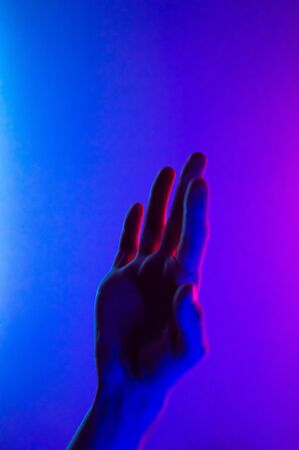 Hands in colorful blue red contrast neon light. Man showing hand palm gesture sign. Vertical orientation photo. Trendy party club style illumination. Space for text. Stylish minimalist backgroundの写真素材