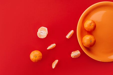 Tangerines on orange plate. Monochrome styled flat lay on bold red background. Fresh citrus fruits.の写真素材
