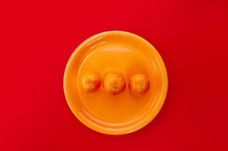 Tangerines on orange plate. Monochrome styled flat lay on bold red background. Fresh citrus fruits.の写真素材