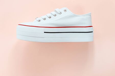 White trendy white sneaker on creamy peach background. Flat lay, top view, shoe side. Place for text. Minimalistic style composition. Sports wear, active lifestyle concept.の写真素材