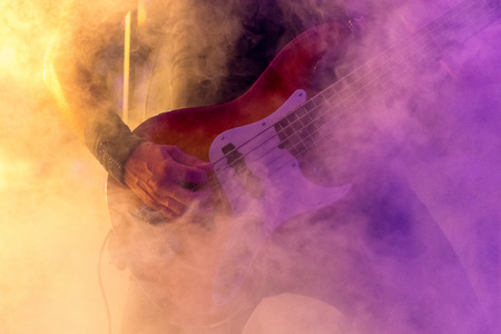 Hand closeup of a bass guitar player during concert, with colored artificial smoke surroundingの写真素材