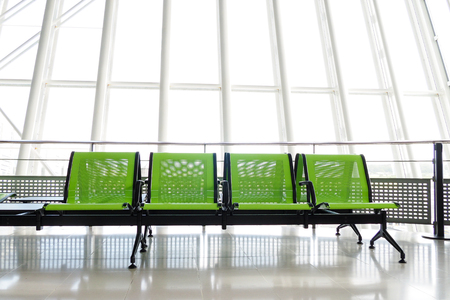 Bench with green seats in the departure hall of an airport, with giant windows in the background.の写真素材