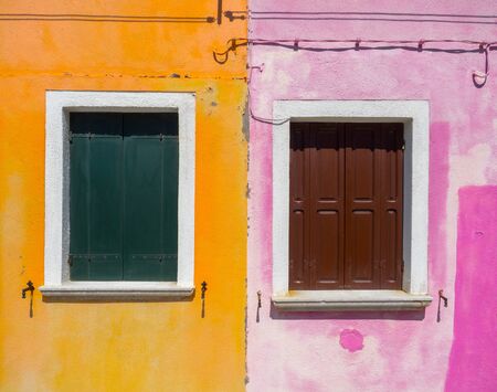 Two windows with wooden screen in colorful pink and orange building facade of Burano town, near Veniceの写真素材