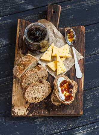 Homemade whole grain bread, cheese and figs jam. Delicious breakfast or snack. On a wooden rustic boardの写真素材