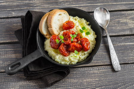 Roasted tomatoes with goat cheese polenta in vintage pan on a dark wooden background. Healthy vegetarian foodの写真素材