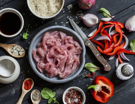 Ingredients for cooking meat stir fry with vegetables and rice - raw meat, sweet red pepper, red onion, rice, spices, on dark wooden background. Top viewの写真素材