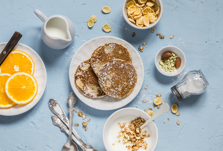 Breakfast table. Whole wheat pancakes, greek yogurt with homemade granola, orange slices, nuts, corn flakes, on a blue stone backgroundの写真素材