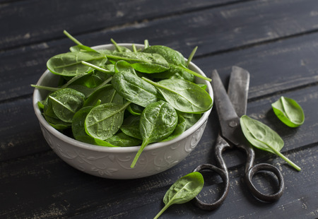 Fresh spinach in a white bowl  and old vintage scissors on a dark wooden background. Healthy foodの写真素材