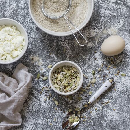 Ingredients for cooking whole grain multi seed bread - whole wheat flour, eggs, ricotta cheese, seeds, on a grey stone background. Baking backgroundの写真素材