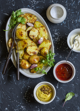 Baked potatoes and sauce him - homemade mayonnaise, ketchup and mustard. Delicious lunch or snack. On dark stone backgroundの写真素材