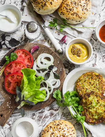 Ingredients for cooking vegetarian burgers - zucchini burgers, homemade buns, tomatoes, onions, herbs, spices and sauces on a light stone background. The view from the topの写真素材