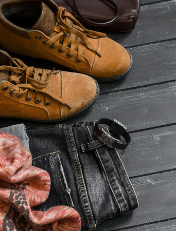 Women's clothing and accessories - boots, jeans, scarf, bag, on dark wood surfaces, vintage styleの写真素材