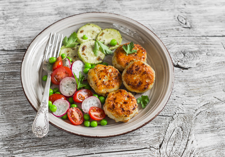 Chicken cutlets,  grilled zucchini  and fresh vegetable salad on rustic light wood backgroundの写真素材