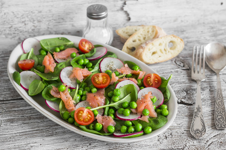 Smoked salmon, spinach, green peas, radish and tomato salad. On light  rustic wooden boardの写真素材