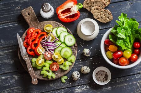 Fresh vegetables - tomatoes, cucumbers, peppers, celery and garden herbs and spices on dark wooden background. Ingredients for fresh vegetable saladの写真素材