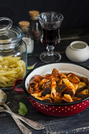Italian pasta with eggplant and tomato sauce and a glass of red wine. On a dark wooden background. Healthy vegetarian foodの写真素材