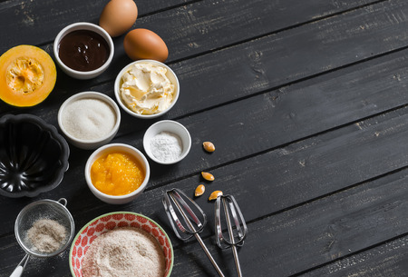 Ingredients to prepare pumpkin cake with chocolate - flour, sugar, pumpkin puree, butter, pumpkin, chocolate, baking dish. On the dark wooden surface.の写真素材