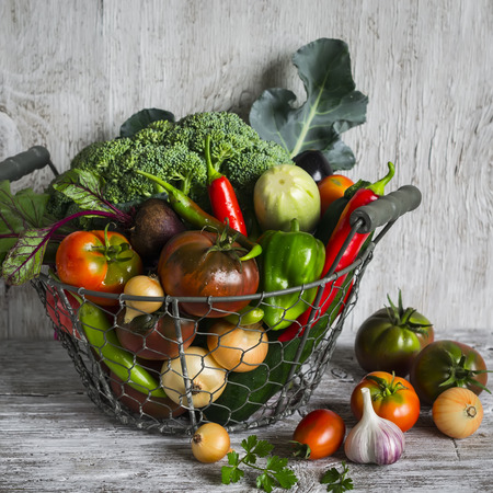 fresh garden vegetables - broccoli, zucchini, eggplant, peppers, beets, tomatoes, onions, garlic - vintage metal basket on a light wooden backgroundの写真素材