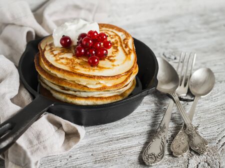 pancakes with honey, sour cream and red currants in a vintage scourage on a light wooden backgroundの写真素材