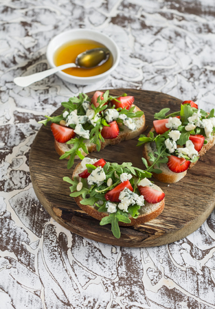 Sandwiches with strawberries, arugula and blue cheese on rustic wooden board on light background. Delicious snack, breakfast or  appetizer with wineの写真素材