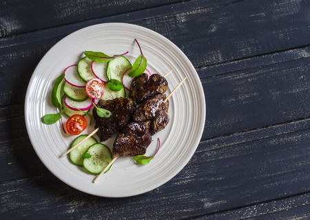 Grilled chicken liver kebabs and fresh vegetable salad on a dark wooden backgroundの写真素材