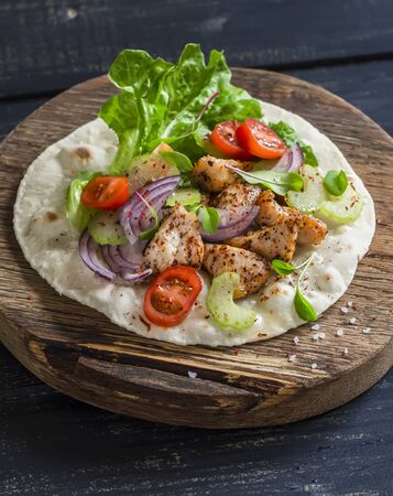 Delicious grilled chicken and fresh vegetables homemade tortilla on a rustic cutting board on a dark wooden backgroundの写真素材