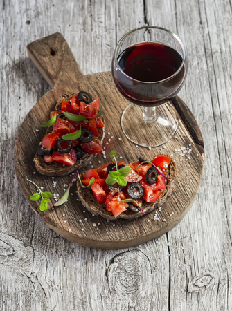 Tomatoes and olives bruschetta and a glass of red wine on rustic wooden backgroundの写真素材