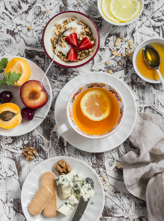 Breakfast or snack table. Lemon tea, fresh fruit, yogurt with granola, blue cheese, biscuits. On a light backgroundの写真素材