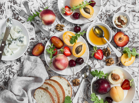 Summer fruits - apricots, peaches, plums, cherries, strawberries and blue cheese, honey, walnuts on a light stone background. Healthy, diet, vegetarian food. Delicious summer dessert or snackの写真素材