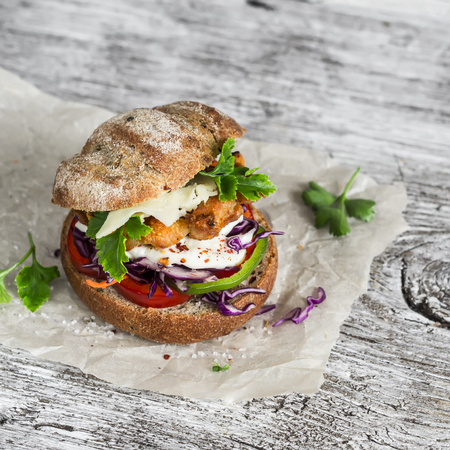 Homemade crispy fish burger on a light rustic wooden boardの写真素材