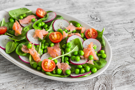Smoked salmon, spinach, green peas, radish and tomato salad. On light  rustic wooden boardの写真素材